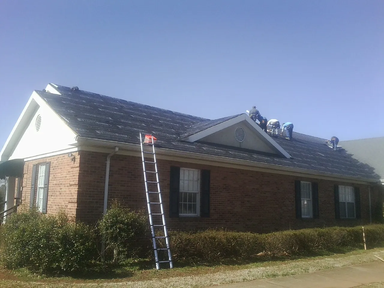 Crew tearing shingles off a brick ranch roof with a ladder set — Emergency Roof Repair work by our crew in Millburn