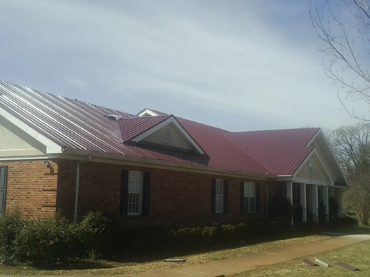 Red metal roof with gabled entries on a long brick building, from a Hail Damage Roof Repair job in Millburn