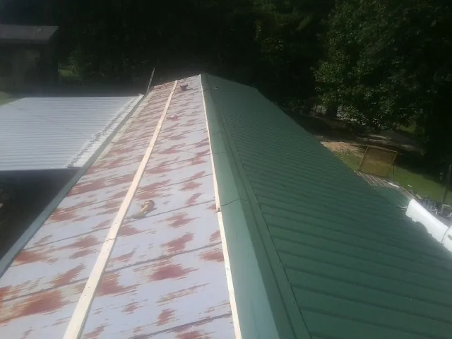 Old rusted panels beside newly installed green metal roofing — Wind Damage Roof Repair by Roofing Brothers in Millburn