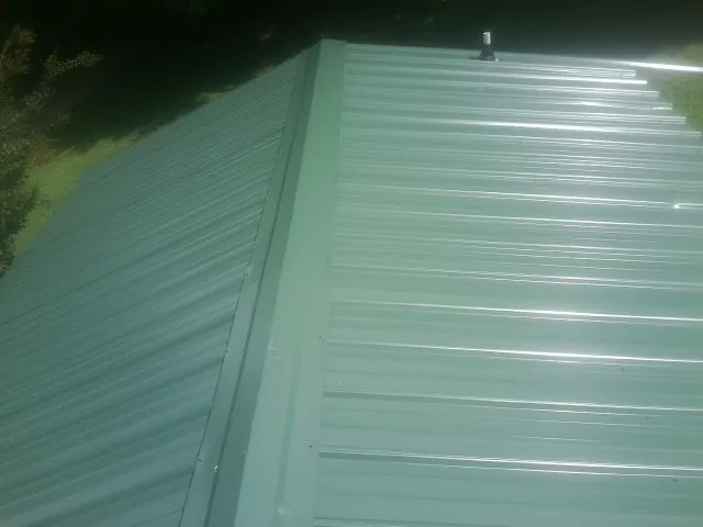 New green metal panels meeting at the ridge of a roof — Flat Roof Repair work by our crew in Millburn