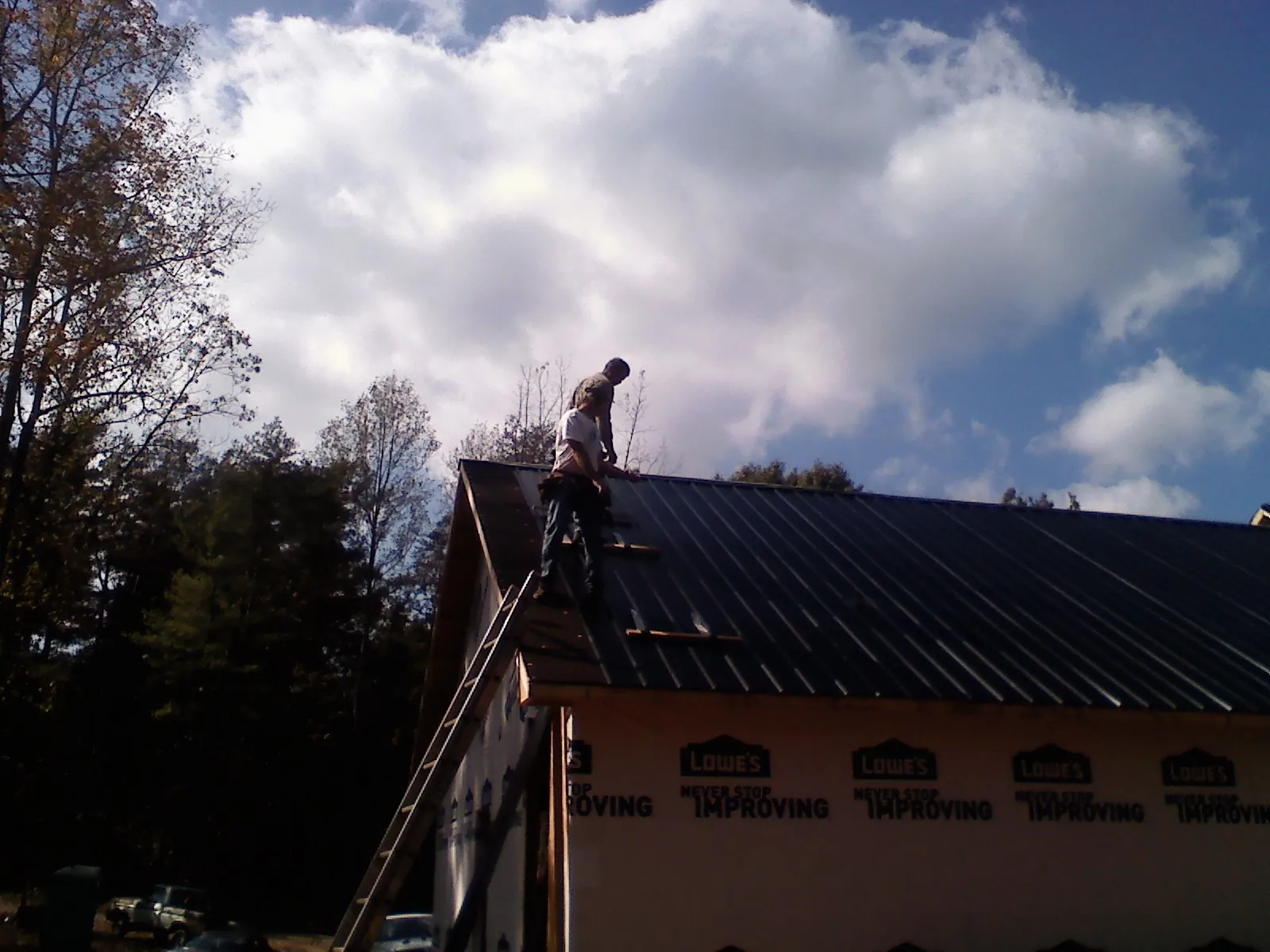 Roofer fastening dark metal panels high against a cloudy sky, from a Roof Inspection job in Millburn