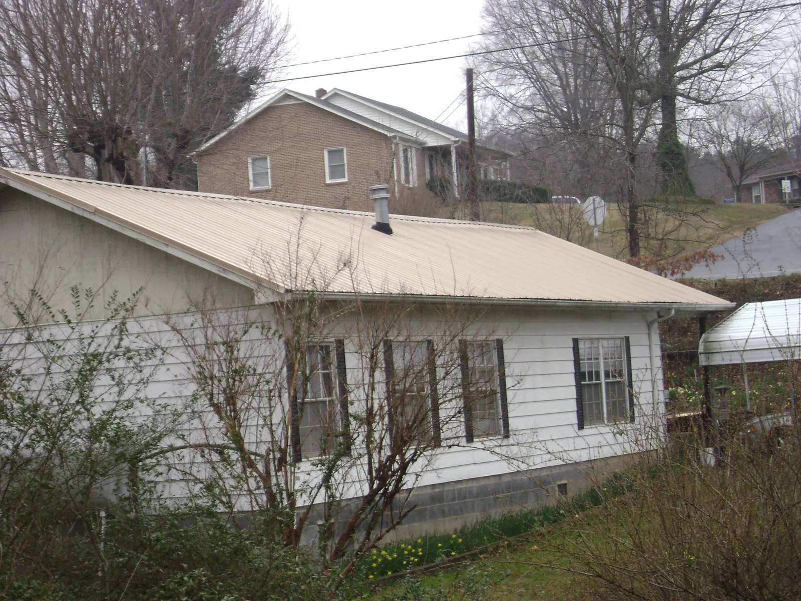 Tan metal roof on a white sided house set into a hillside — Commercial Roofing by Roofing Brothers in Millburn